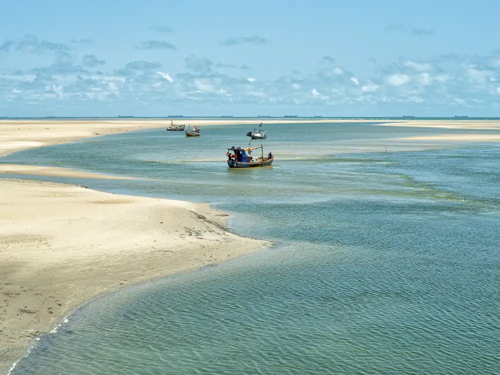 Coroas de areia e o mar verde em Raposa, com barcos de pesca ao fundo